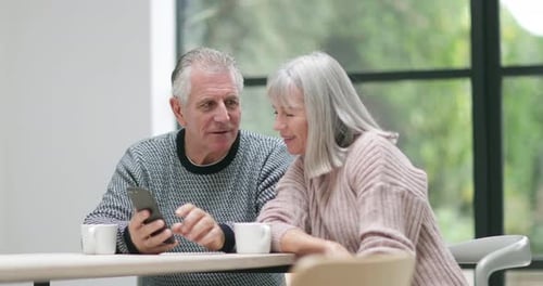 Senior Couple Using Smartphone Together at Table Indoors