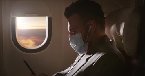 Man in Face Mask on Airplane at Sunset