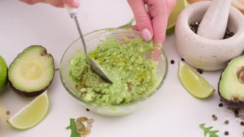 Woman Mashing Avocado for Guacamole in Glass Bowl