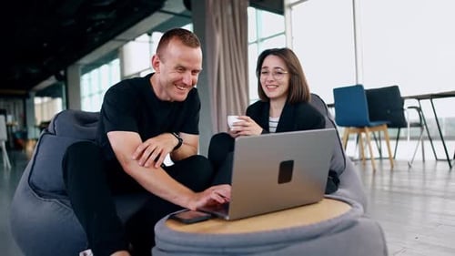 Deux collègues diversifiés sont assis à discuter et à rire dans des chaises confortables.