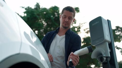 Man recharging battery for electric car during road trip. Exalt