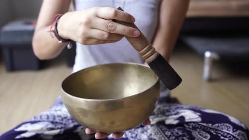 Woman plays singing bowl indoors close up