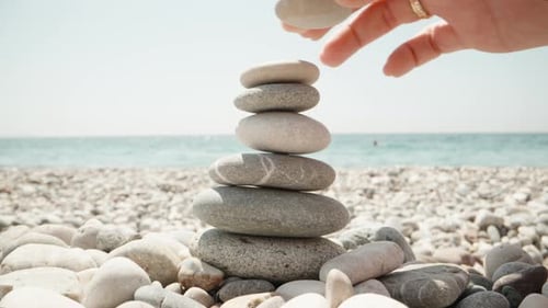 Close-up, a woman makes a cairn. Handmade stone tower on the seashore. A stack of balanced pebbles o