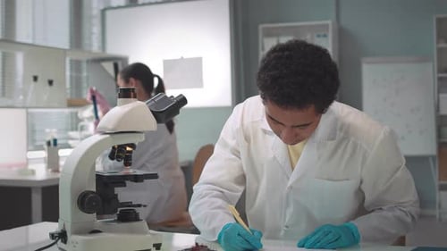 Young Scientist Analyzing Sample with Microscope in Lab
