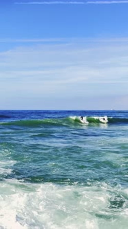 Surfers Waiting and Riding Waves on Ocean Shore on Sunny Day Under Clear Blue Sky