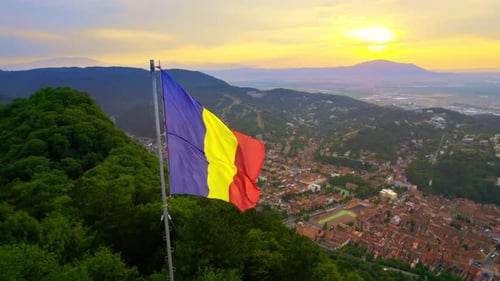 Romanian Flag Waving Over Mountain Town at Sunset