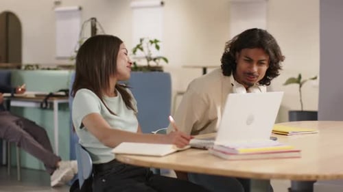 Deux étudiants travaillant dans un centre d'études, un homme s'approche pour discuter d'un ordinateur portable tandis qu'une femme écrit des notes