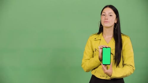 A Young Caucasian Woman Shows a Smartphone with Green Screen to the Camera Green Screen