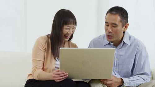 Smiling couple sitting using laptop on the couch