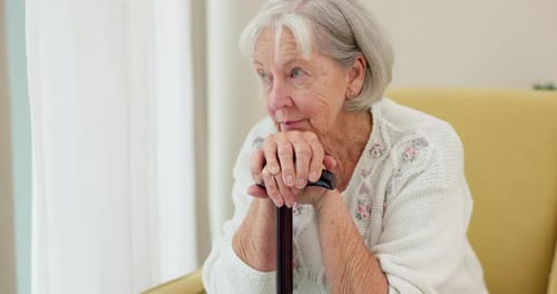 Senior Woman Sitting With Cane Looking Out Window