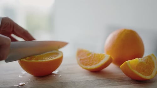 Nahaufnahme von Hand, wie frische Orange auf einem Holzschneidebrett von Hand geschnitten wird