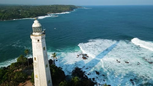 Drone Classic White Lighthouse Tropical Forest Standing Against Crashing Ocean Waves Clear Blue Sky