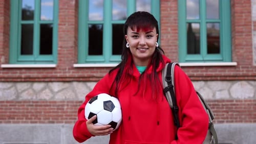 Young female soccer player holding ball in front of school