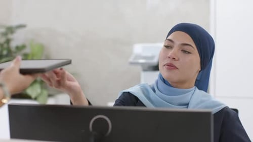 O visitante está estendendo o tablet enquanto a recepcionista está se inclinando para revisar a fatura para confirmar na recepção