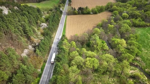 Camera follows truck driving along a county road running between forested hills and agricultural fie
