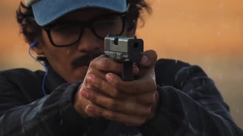 Man firing gun shots towards camera at desert shooting range, slow motion