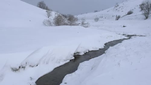 Winterbach, der durch die verschneite Hügellandschaft fließt. Kleiner Gebirgsfluss, der durch eine