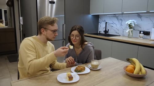 Affectionate Young Couple Feeding Each Other Breakfast in Kitchen