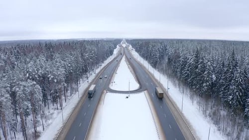 Car traffic on the highway among the trees in the snow. Drone point of view