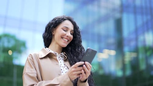 Close up. Young smiling businesswoman is using a smartphone while standing on the street near
