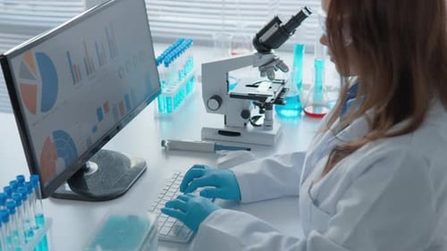 Female Scientist in Modern Laboratory Working on Computer and Analyzing Samples with Microscope