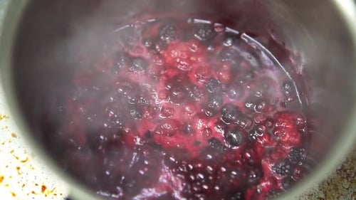 Close up of red berries, blackberries and blueberries being cooked in slow motion in a pot. Smoke co