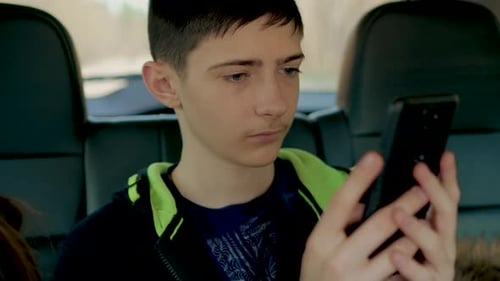 Bored Teen Boy in Car Playing on Smartphone While Traveling with Parents