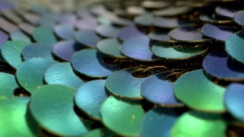 Vue macro d'un ensemble de paillettes bleues, sarcelles et vertes plates et réfléchissantes. Les paillettes commencent
