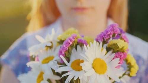 Blonde Girl Holds a Bouquet of Flowers Stands in a Meadow at Sunset Closeup Shot