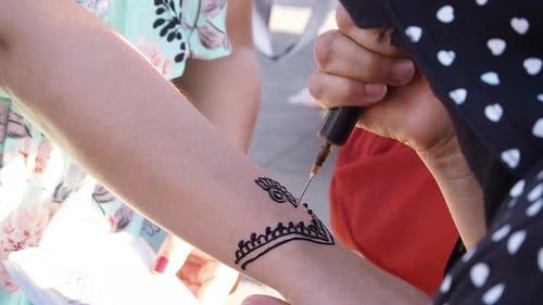 Artist applies henna tattoo to customer's arm
