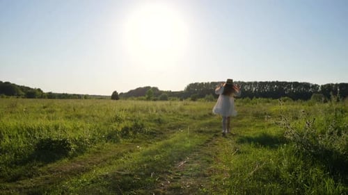 Rear View of Unrecognizable Cheerful Woman in Straw Hat and White Dress Joyfully Running Bouncing