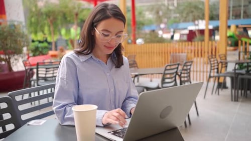 Smiling Woman Freelancer Using Laptop at Outdoor Cafe