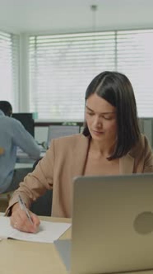 Businesswoman Using Laptop and Writing Down Notes in Office