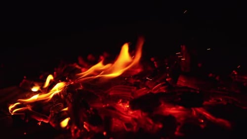 Moving the smoldering embers of burning out campfire with a stick.