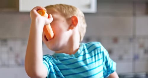 Child Eats Carrot Stick in Kitchen Close Up
