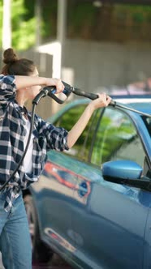Amidst the Car Wash Setting a Gorgeous Girl is Employing a Highpressure Water Gun to Clean a Car