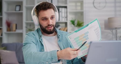Homme concentré portant des écouteurs, tenant un appel vidéo avec des clients devant un ordinateur. Professeur de sexe masculin parlant