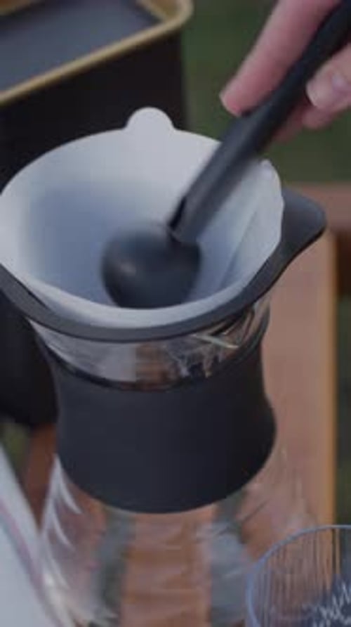 Hand Adding Ground Coffee to Paper Filter in Dripper on Wooden Table