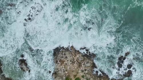 Aerial Video of Ocean Waves Crashing Against Rugged Rocky Shoreline With White Foam Exploding Into
