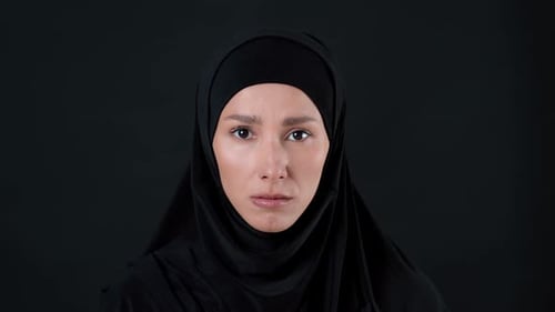 Frau im schwarzen Hijab blickt direkt in die Kamera vor dunklem Hintergrund
