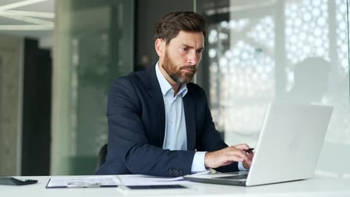 Busy financier in formal suit making financial calculations using calculator, typing on a laptop