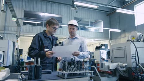 Engineer in Hard Hat and Factory Worker are Talking about Blueprint