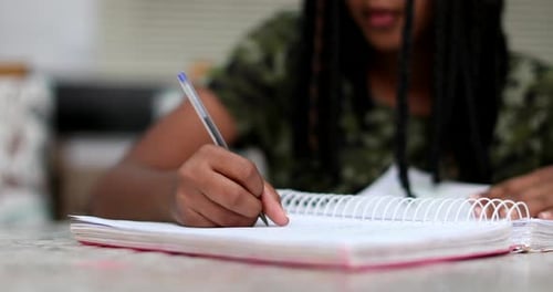 Girl Writes in Notebook at Table Indoors