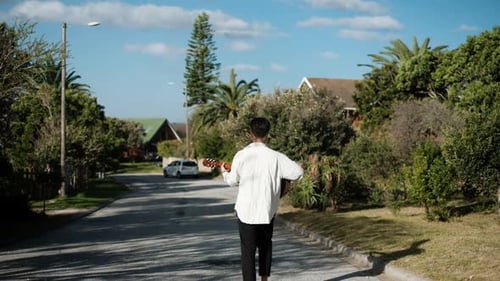 Young Man Walking Down A Street While Playing An Acoustic Guitar