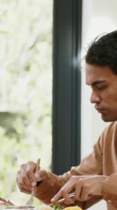 Vertical video: Cutting brown shirt man starting meal, eating with fork, knife at home, copy space