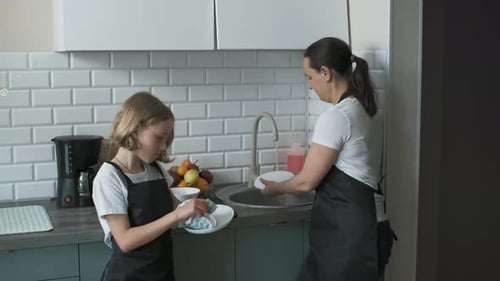 Girl and Woman Washing Dishes Together in Kitchen