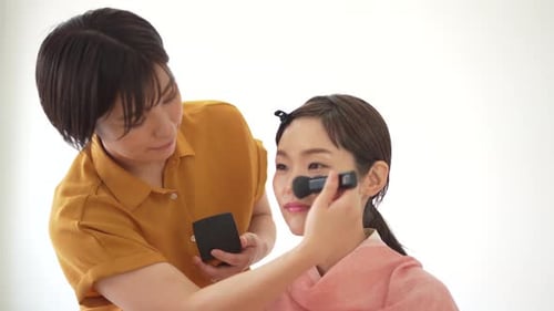 Woman Applying Makeup to Smiling Young Woman