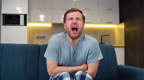 Man Clutching Stomach on Couch in Apartment