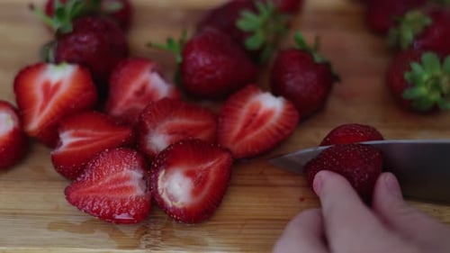 strawberries on wooden board in kitchen. knife cutting one strawberry fruit. slice of berry close up