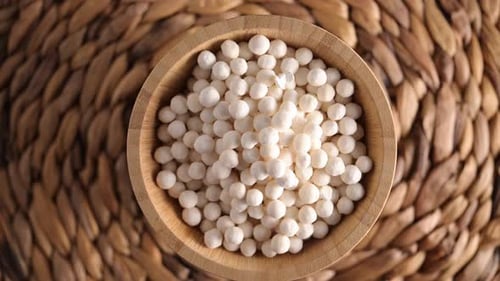 White dry tapioca pearls in wooden bowl rotating on wooden background.